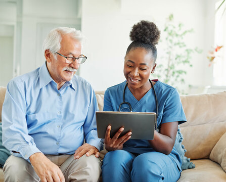 nurse doctor senior care tablet computer technology showing caregiver help assistence retirement home nursing elderly woman african american black happy laughing man