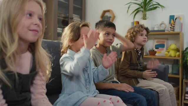 Side footage of Caucasian kids sitting on couch and repeating moves after offscreen play assistant during birthday party at home