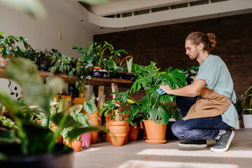 Handsome male business owner working, arranging and gardening houseplants at his florist shop indoor.