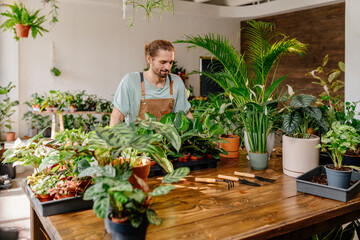 Caucasian man checks the condition of plants, for sale in her decorative plant shop. Gardener working in flower shop, plant store. Business, people and houseplants concept.