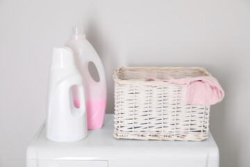 Baby clothes in wicker basket and laundry detergents on washing machine near light wall