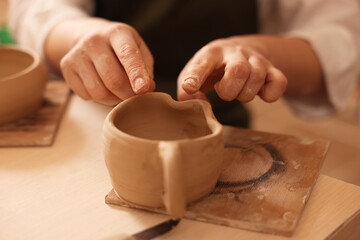 Fototapeta na wymiar Pottery crafting. Woman sculpting with clay at table, closeup