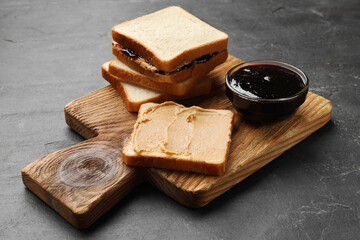 Tasty peanut butter sandwiches and jam on dark gray table