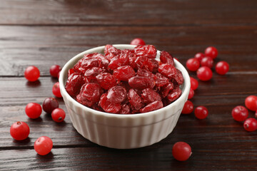 Tasty dried cranberries in bowl and fresh ones on wooden table, closeup