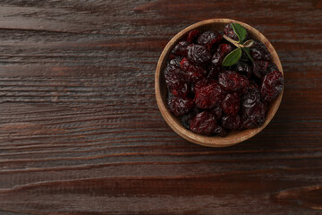 Tasty dried cranberries in bowl on wooden table, top view. Space for text