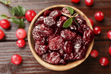 Tasty dried cranberries in bowl, fresh ones and leaves on wooden table, top view