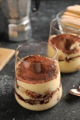 Delicious tiramisu in glasses on grey textured table, closeup