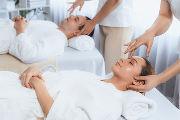 Caucasian couple enjoying relaxing anti-stress head massage and pampering facial beauty skin recreation leisure in dayspa modern light ambient at luxury resort or hotel spa salon. Quiescent