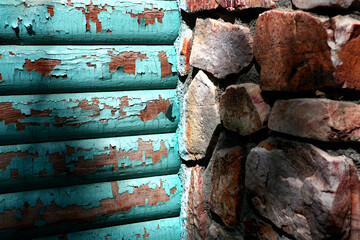 Close-up of a log cabin exterior wall with peeling turquoise paint and a stone fireplace.