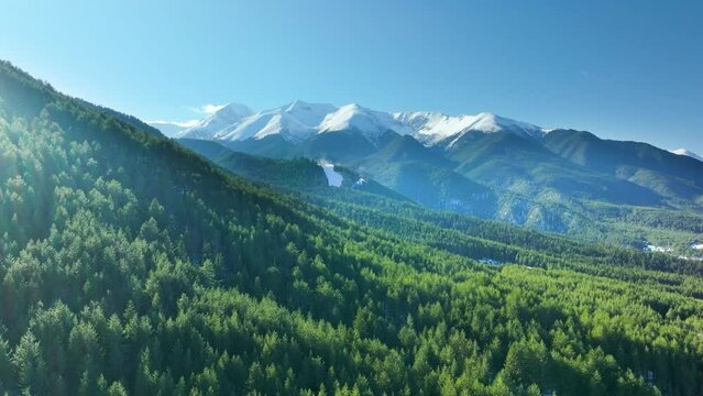 Aerial drone shot, flying from behind forest covered mountain slope to reveal beautiful snowy peaks of the Pirin region in Bulgaria.