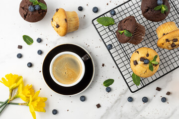 Cup of hot coffee, fresh baked muffins with chocolate chips, blueberry berries and mint leaves on...