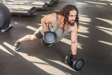 Portrait of muscular athletic man with long curly hair working out in gym, standing in plank...