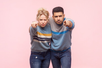 Obraz premium Portrait of angry irritated woman and man standing pointing together at camera arguingg with somebody expressing hate. Indoor studio shot isolated on light pink background.
