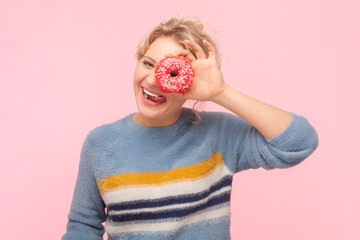 Portrait of funny playful positive blonde woman wearing sweatshirt covering her eye with tasty...