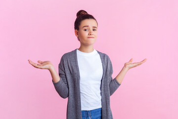 Portrait of confused teenage girl with bun hairstyle in casual clothes standing with shrugging...