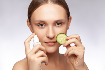 Closeup portrait of adorable beautiful woman holding facial lotion and slice of cucumber skin care...