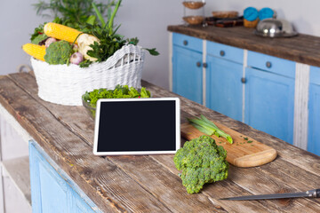 Tablet with empty display, fresh vegetables and cooked salad on wooden table in modern kitchen, online cooking tips for healthy vegetarian diet, food recipes, menu and blog.