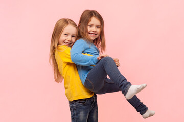 Portrait of two playful cute positive little girls having fun together, playing active games, expressing joy and happiness. Indoor studio shot isolated on pink background. - obrazy, fototapety, plakaty