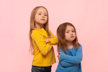 Portrait of two serious strict proud funny little girls standing with crossed hands, looking at...
