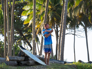 Surfer, man stretching on the beach with surfboard for ocean waves.