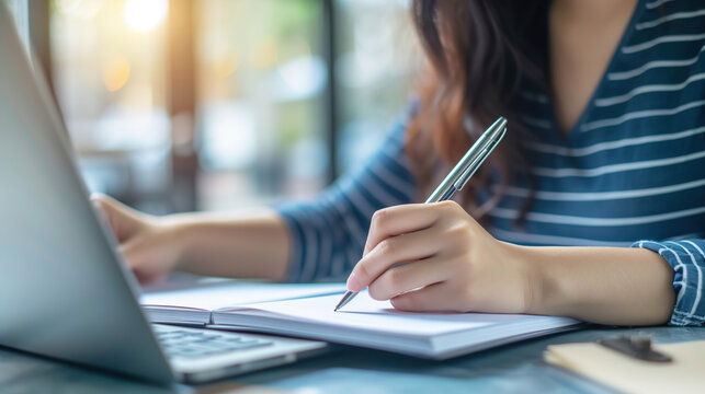 Close up of business woman hand with a pen writing on paper notebook, planning event schedule. Female student online studying on laptop, searching the information, e-learning, online study concept