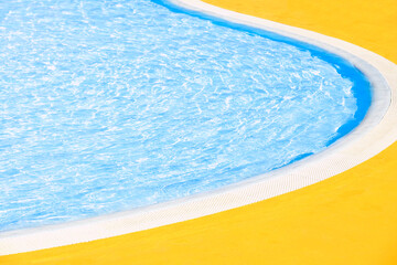 Outdoor swimming pool edge with curved border in sunny summer day. Clear blue water and yellow floor.