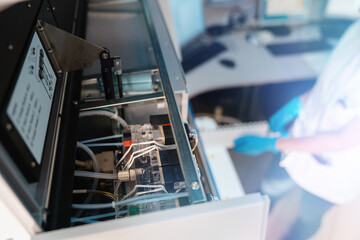 Focus on a machine part in a laboratory while medical professional is putting in a rack with test...