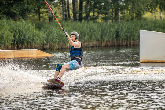 Ypung man wakeboarding and doing different board tricks. Wake boarding sportsman man jumping high wake boarding raley trick with huge water splash in the cable park