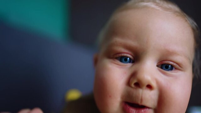 Chubby face of a cute Caucasian blue-eyed baby. Close up. Curious infant trying to get a camera.