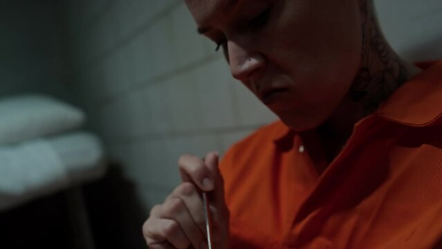 Close up view of disgusted female inmate eating oatmeal from steel bowl while sitting in prison cell