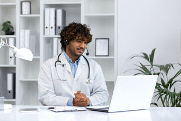 Confident ethnic doctor providing virtual healthcare services in a modern clinic setting, using a...
