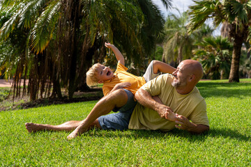 family and love concept - young father tickling his little son in park. dad tickles his son's legs...