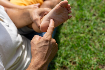 family and love concept - young father tickling his little son in park. close-up of a child's heel and the father's hand who tickles him. cheerful baby laughs from being tickled - obrazy, fototapety, plakaty