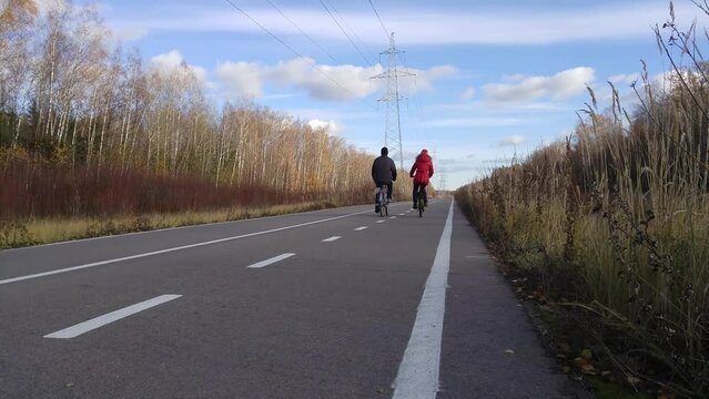 Man and woman ride on bicycle on asphalt road in autumn park