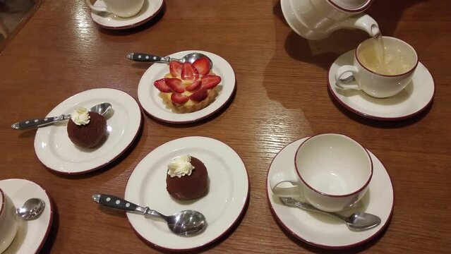 Hands pour tea on cups on table with plates and cakes, mobile phone video.