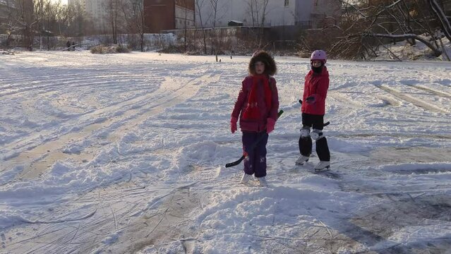 Two girls with sticks come to hockey puck and one take it on pond
