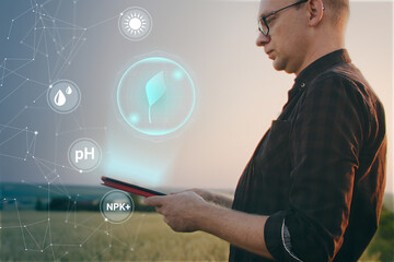Farmer using digital tablet in wheat field with smart farming interface icons. Smart and new...