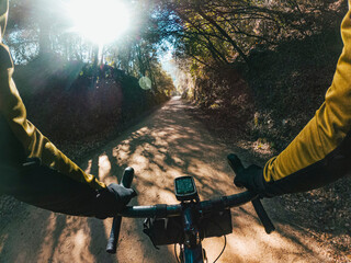 Riding a gravel bike with dorp handlebar between wood forest trees on a gravel path with sun flare...