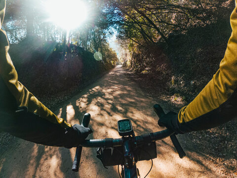 Riding a gravel bike with dorp handlebar between wood forest trees on a gravel path with sun flare shining through the branches