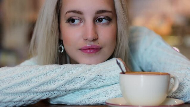 Young blonde with head on hands looks around and on coffee cup near on table