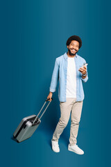 Full length of young, modern man with a suitcase and smartphone depicts the intersection of technology and travel. This image conveys a sense of forward movement and the ease of modern journeys.