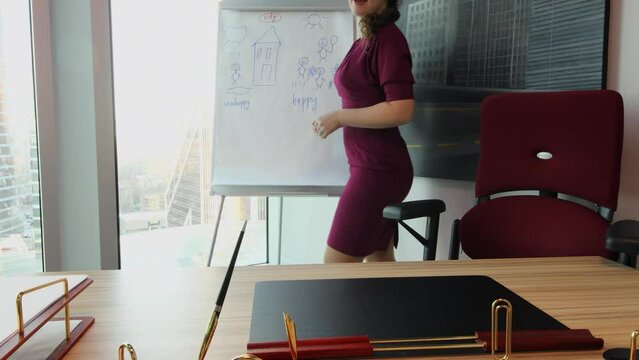 Woman stands up from chair and goes to draw board with simple illustrations