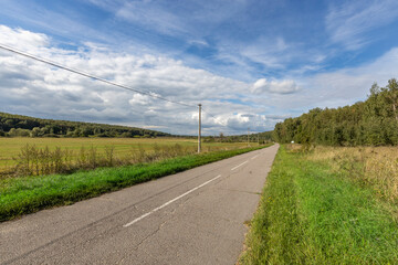 Fototapeta na wymiar road in the countryside, bright sunny afternoon, an asphalt road along which there is an electric wire on concrete supports