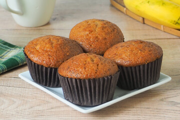 Banana muffins, close-up of the front, on a wooden table, with bananas and coffee cups in the background.