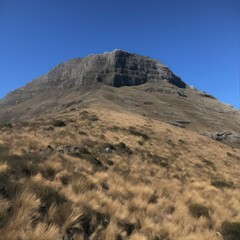 a mountain with grass and blue sky - obrazy, fototapety, plakaty