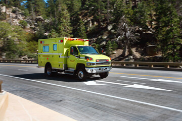 A Yellow Fire Rescue Paramedic First Responder Ambulance racing down a mountain road with emergency lights flashing.
