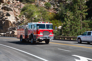 Fototapeta na wymiar A red firetruck with emergency lights flashing passing cars as it races down a mountain road.