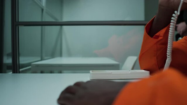 Close up view of hand of unrecognizable Black inmate sitting at table in visiting room and taking landline phone for conversation