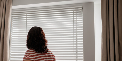 Fototapeta premium Woman Looking Out of Window Blinds