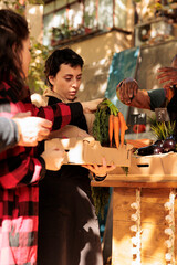 Team of vendors selling fresh fruits and veggies in boxes, serving elderly man and young woman at local farmers market. Smiling people looking at healthy organic colorful products.